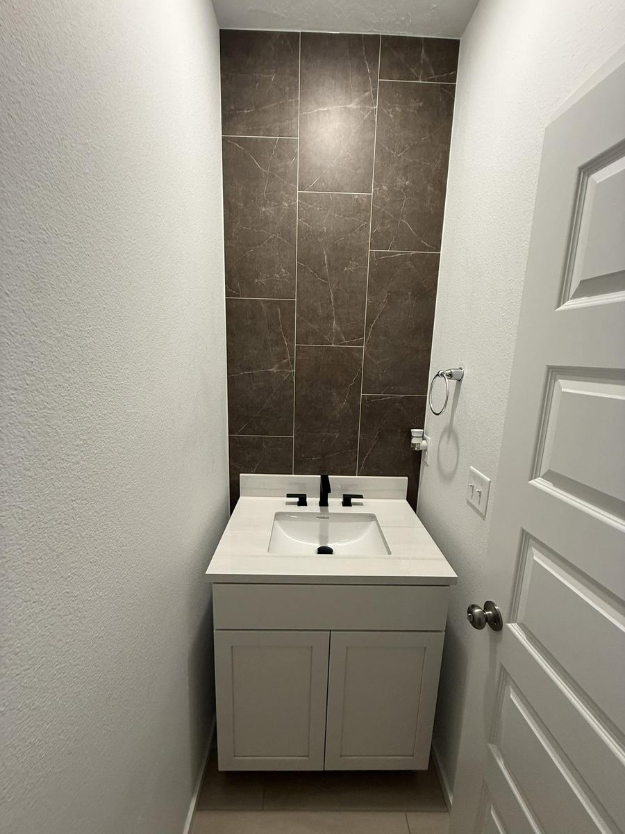 Finished half bathroom with a full-height tiled accent wall behind a white vanity and black fixtures
