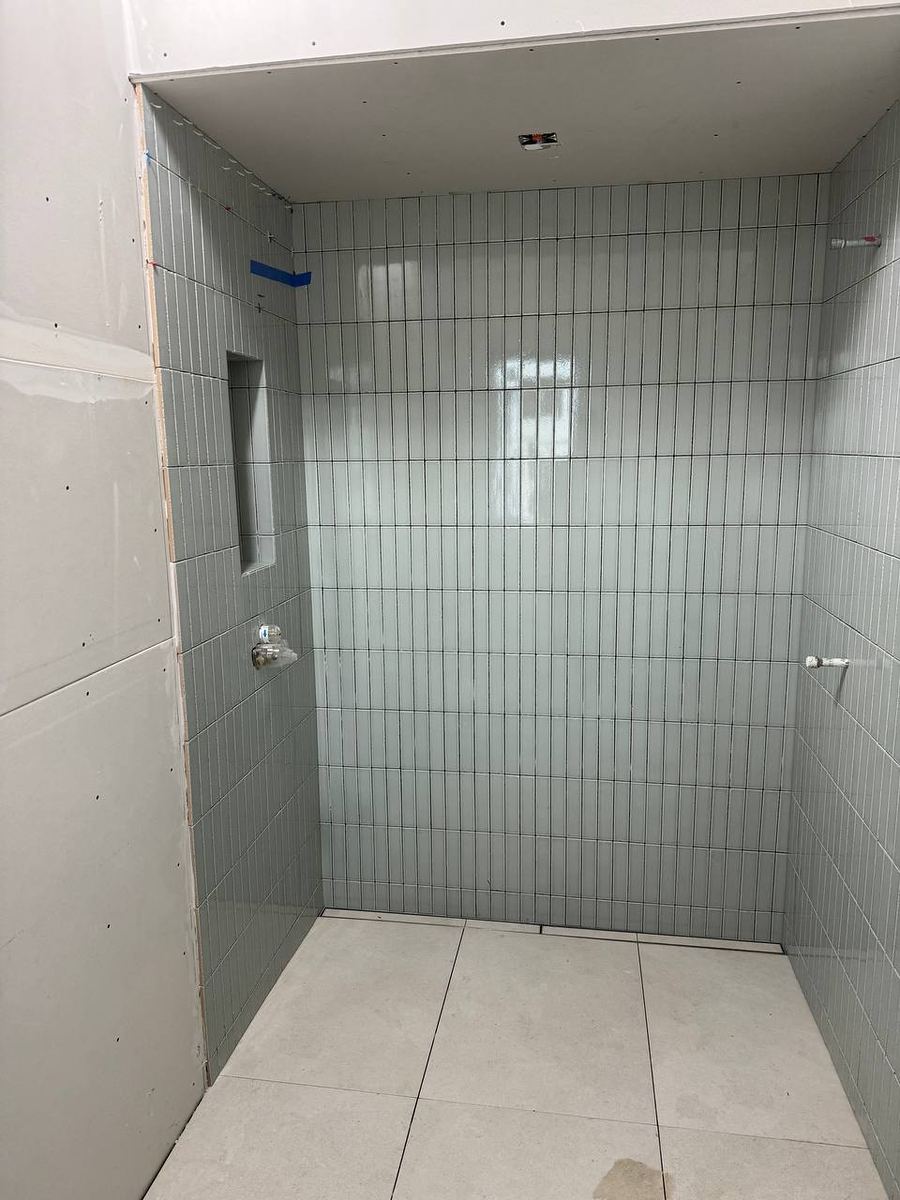 Shower alcove tiled in sage green vertical stacked tile with a recessed niche and large-format floor tile