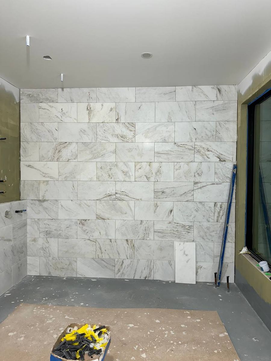 Bathroom feature wall tiled floor to ceiling in white marble-look porcelain laid in a running bond pattern