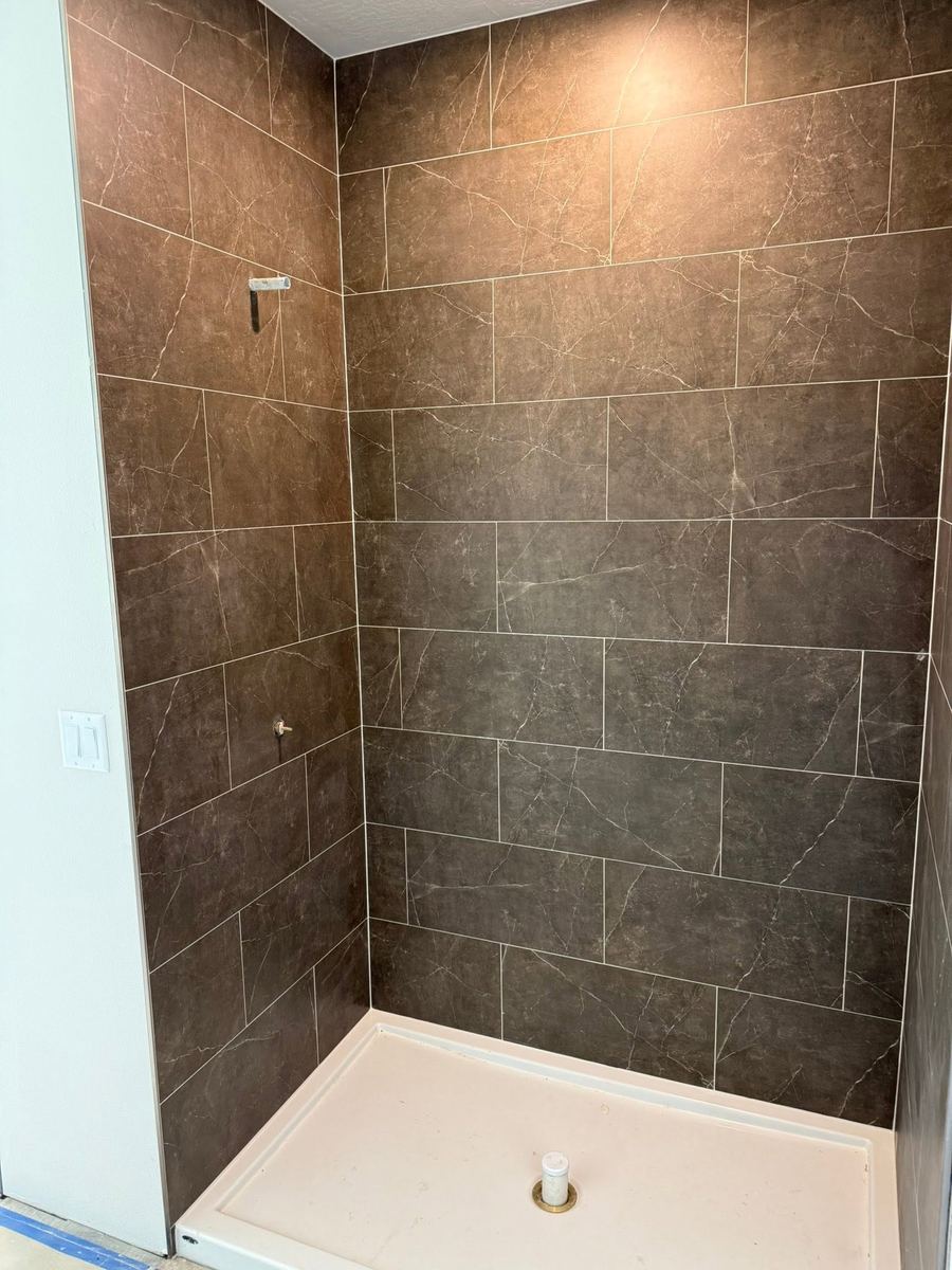 Shower surround tiled in large-format brown marble-look porcelain with tight straight grout lines